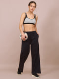 A woman wearing a sports bra and track pants, holding a soccer ball, standing against a beige background.